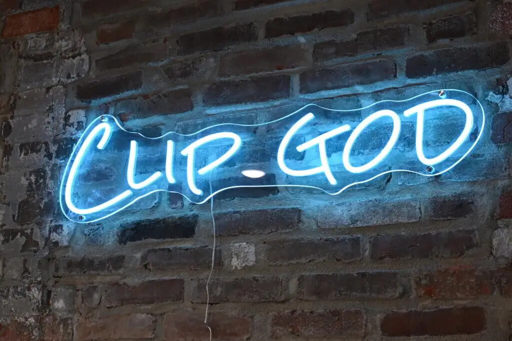 A blue neon sign on a brick wall that says Clip God